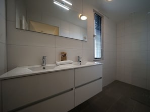 Een moderne badkamer met een dubbele wastafel, een grote spiegel en een raam met zonwering.