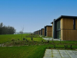 Een rij moderne gebouwen met platte daken, een grasveld op de voorgrond en een heldere lucht.