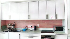 A kitchen with white cabinets, a pink brick backsplash, a sink, a dish rack, a kettle, a toaster, and a stove. - Spacious Double Room with Garden & Parking – Suitable for male or Couple (Wicklow)