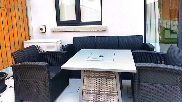 A patio area with a white table, black wicker furniture, a window, and a white air conditioning unit. - Spacious Double Room with Garden & Parking – Suitable for male or Couple (Wicklow)