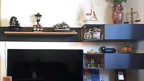 A living room with a large flat-screen TV, shelves with various decorative items, and a vase with flowers on the wall. - Spacious Double Room with Garden & Parking – Suitable for male or Couple (Wicklow)