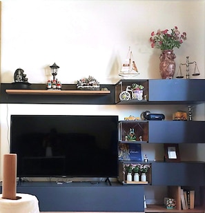 Olohuone, jossa on suuri taulutelevisio, hyllyjä, joissa on erilaisia koriste-esineitä, ja seinällä oleva maljakko, jossa on kukkia.