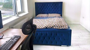 A bedroom with a bed, a desk with a keyboard, a chair, and a window with a view of a road and greenery. - Spacious Double Room with Garden & Parking – Suitable for male or Couple (Wicklow)
