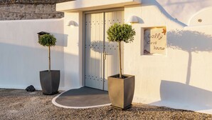 Une entrée d’immeuble avec une porte blanche, deux arbres en pot et une enseigne indiquant « Celly Cave House ».