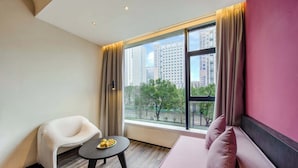 A modern hotel room with a large window, a sofa, a chair, and a small table with fruit. - M Hotel (Hangzhou)