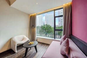 A modern hotel room with a large window, a sofa, a chair, and a small table with fruit. - M Hotel (Hangzhou)