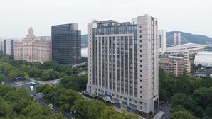 A high-rise building with a modern glass facade, surrounded by greenery and other buildings. - M Hotel (Hangzhou)