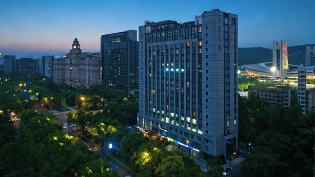 A high-rise building with multiple floors, surrounded by trees and other buildings. - M Hotel (Hangzhou)