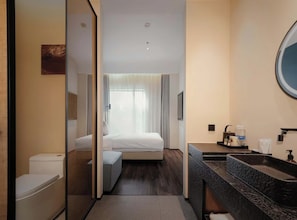 A hotel room with a bed, a toilet, a sink, and a mirror. - M Hotel (Hangzhou)