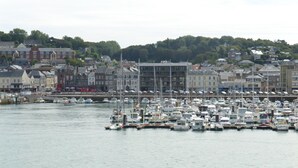 A marina with numerous boats docked, surrounded by buildings and a hilly backdrop. - Large family home in Normandy (Ganzeville)