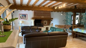 A living room with a brick fireplace, leather sofas, a dining table, and a wooden ceiling. - Large family home in Normandy (Ganzeville)