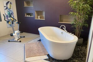 Une salle de bain moderne avec une baignoire sur pieds, du matériel de fitness et des étagères décoratives.