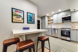 Una cocina moderna con barra, electrodomésticos de acero inoxidable y dos carteles enmarcados de motivos viajeros en la pared.