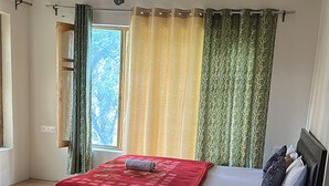 Une chambre à coucher avec un lit, un ventilateur de plafond, une fenêtre avec des rideaux et un plancher en bois.