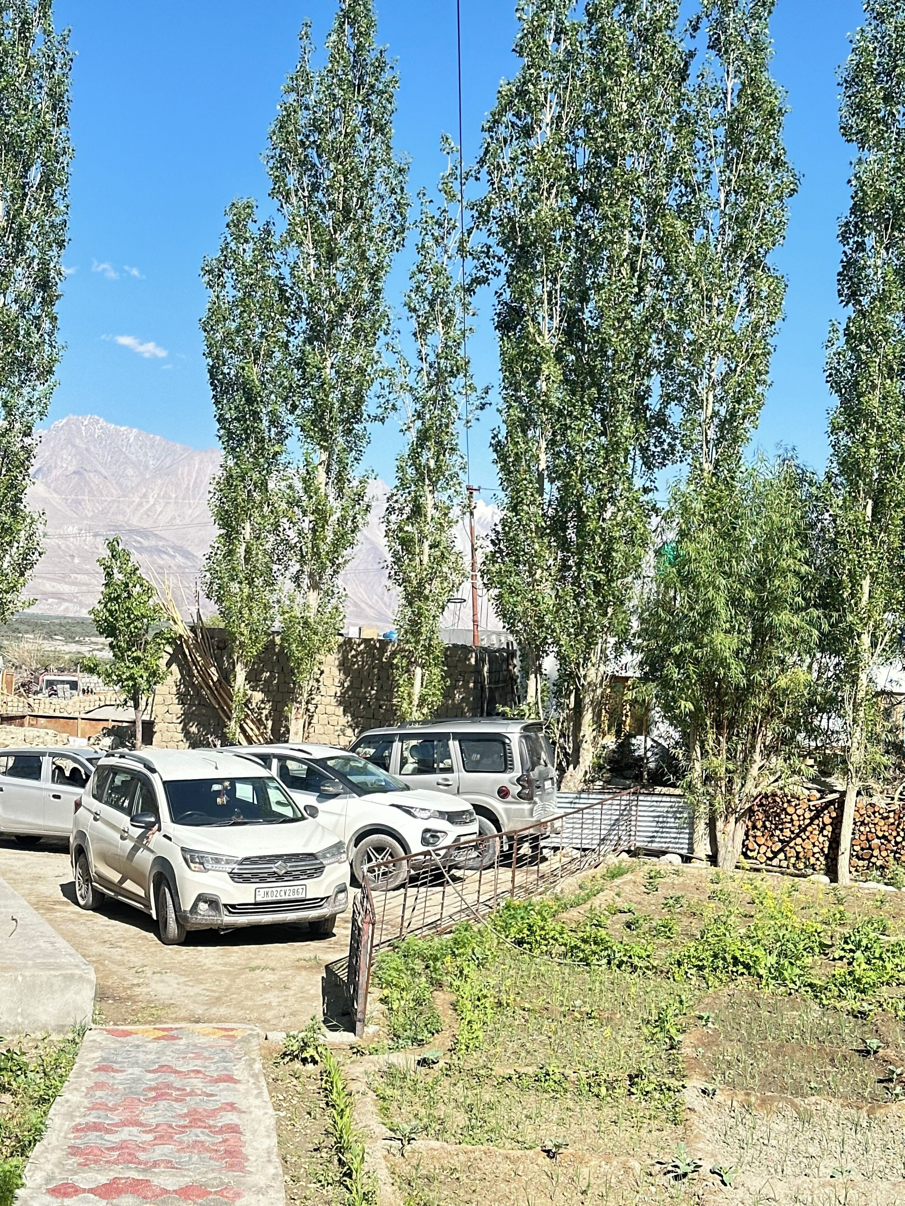 Uma área de estacionamento com vários carros, um caminho que leva a um edifício e montanhas ao fundo.