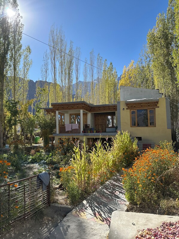Un edificio de dos pisos con balcón, rodeado de un jardín con diversas plantas y flores.