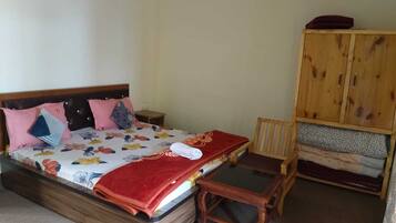Un dormitorio con cama, mesita de noche de madera, una silla de madera, una pequeña mesa y un armario de madera.