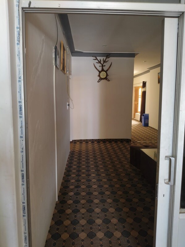 A hallway with patterned flooring, a wall-mounted clock, and a door leading to another room.