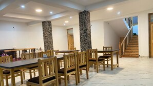 Un espace repas avec des tables et des chaises en bois, un pilier en pierre et un escalier.