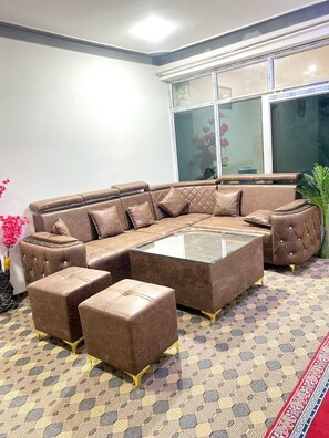 A modern living room with a sectional sofa, ottomans, and a glass coffee table. - Feroz - HomeStay (Leh)