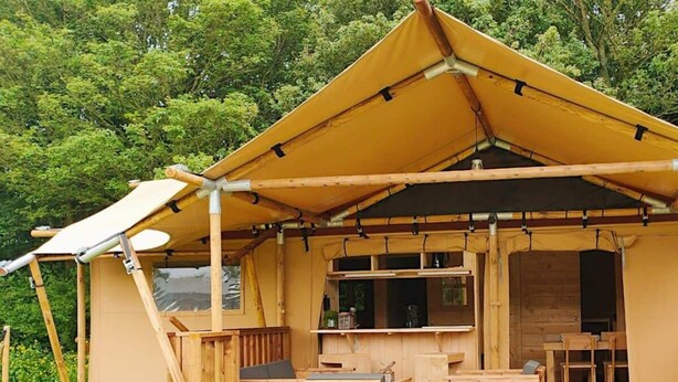 A wooden cabin with a covered deck, a dining area, and a kitchen. - Holiday Home in Noord-scharwoude With Wi-fi (Noord-Scharwoude)