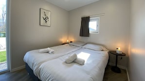 A double bed with white linens, a bedside table with a candle, a framed artwork on the wall, and a window with a curtain. - Holiday Home in Dordrecht With Terrace (Dordrecht)