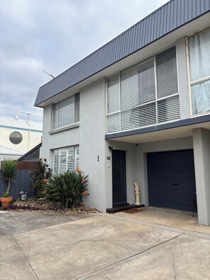 Una casa moderna a due piani con garage, un piccolo giardino e un vialetto in cemento.