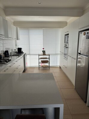 A modern kitchen with white cabinets, a stainless steel refrigerator, and a central island. - Edithvale Beach House (Edithvale)