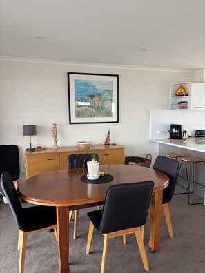 A dining area with a wooden table, black chairs, a potted plant, and a framed painting on the wall. - Edithvale Beach House (Edithvale)