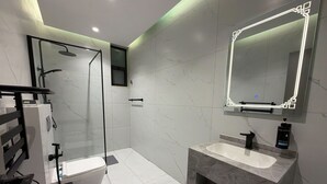 A modern bathroom with a glass shower enclosure, a toilet, a sink with a marble countertop, and a large mirror with a lighted frame. - 405 tara-JRE Jabal Al Lweibdeh with stunning view (Amman)