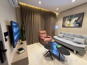 A modern living room with a flat-screen TV, a sofa, a pink chair, a coffee table, and a large painting on the wall. - 405 tara-JRE Jabal Al Lweibdeh with stunning view (Amman)