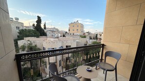 Un balcon avec deux chaises et une table, d’où l’on peut admirer un paysage urbain composé d’immeubles et d’arbres.