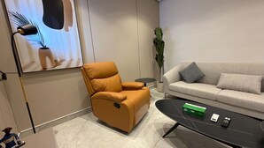 Un salon moderne comprenant un canapé, un fauteuil inclinable, une table basse, une plante et un tableau encadré.