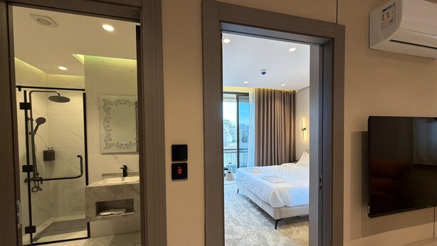 Une chambre d’hôtel moderne dotée d’une douche en verre, d’un lit, d’un téléviseur fixé au mur et offrant une vue sur la ville.