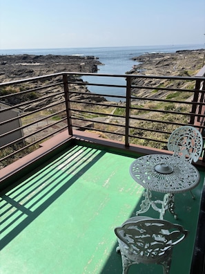 Un balcón con piso verde, baranda de metal y dos sillas blancas ornamentadas.