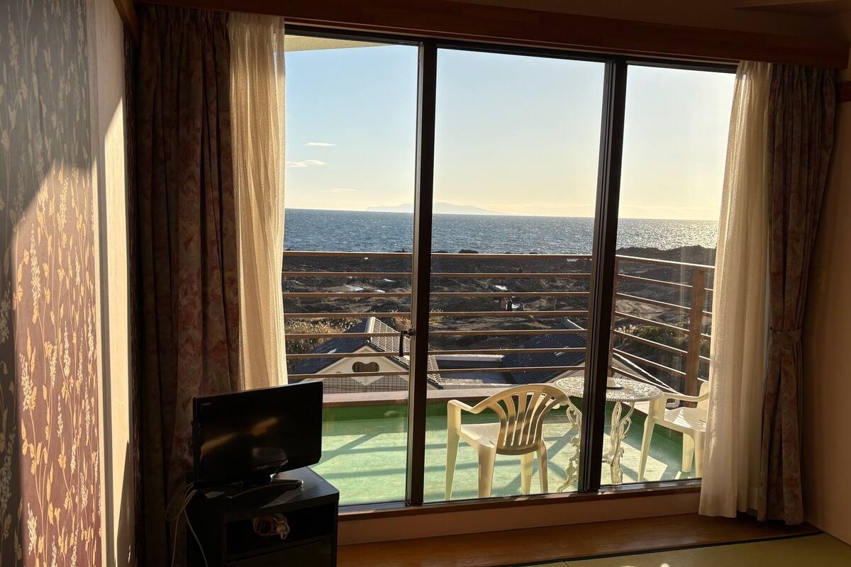 A room with a large window, a television, a chair, and a wooden table.