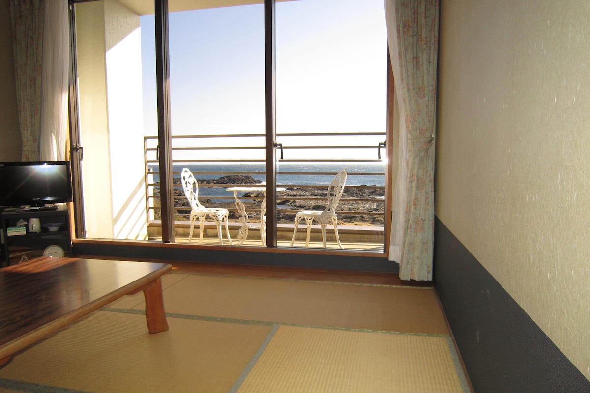 A room with a large sliding glass door leading to a balcony with a view of the ocean.