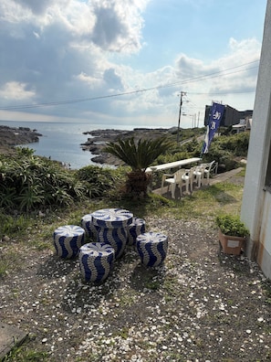 Une vue sur la côte, avec un rivage rocheux, un palmier et un espace aménagé avec des chaises et une table.