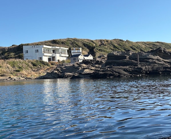 Un bâtiment situé sur la côte, doté de nombreux balcons, qui se trouve sur un littoral rocheux, avec une eau bleu clair en premier plan.