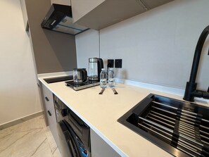 A modern kitchen with a built-in dishwasher, a coffee maker, and two water bottles on the counter. - 413 tara-JRE Jabal Al Lweibdeh with stunning view (Amman)