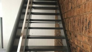 Uma escadaria com guarda-corrimão de metal, parede de tijolos e piso de azulejos.