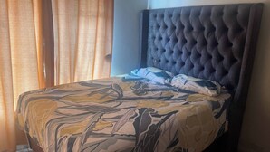 Quarto com cabeceira estofada, colcha estampada e cortinas.
