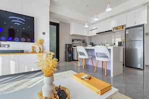 A modern kitchen with a built-in TV, white cabinetry, and a stainless steel refrigerator. - Serene 1-Bedroom Apartment with National Park Views (Nairobi)