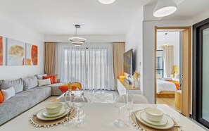 A modern hotel room with a dining area, a sofa, a TV, and a large window with curtains. - Serene 1-Bedroom Apartment with National Park Views (Nairobi)
