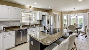 Uma cozinha moderna com armários brancos, bancada de granito, eletrodomésticos de aço inoxidável e uma área de refeições com cadeiras e mesa.
