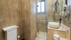 Et badeværelse med toilet, glasbrusekabine, vask og spejl.