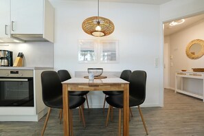 Una cocina moderna con zona de comedor, que incluye un horno empotrado, una cafetera y una mesa de comedor con sillas.