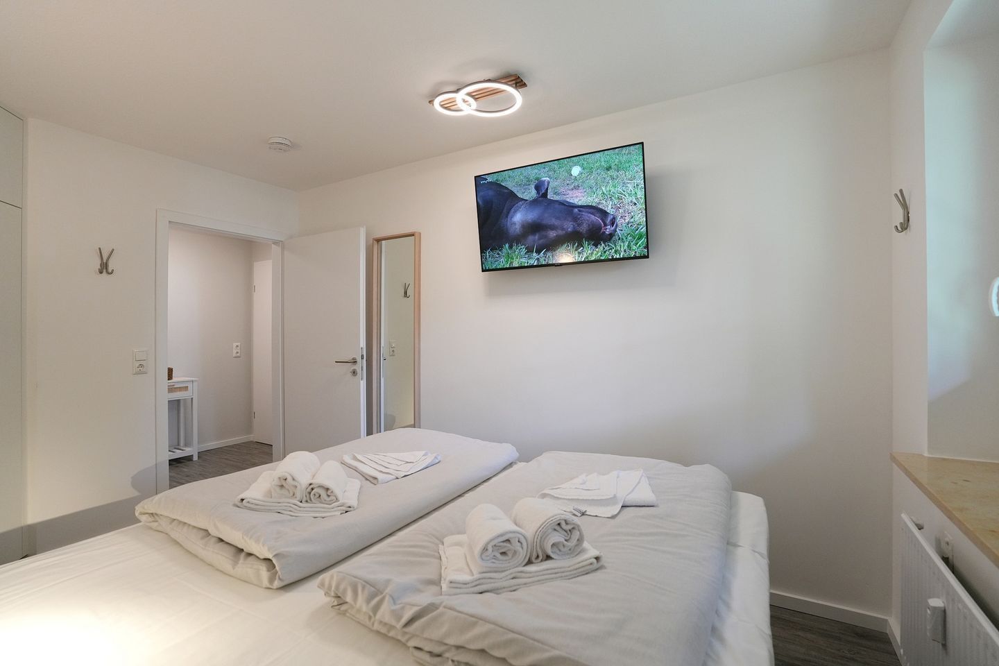 A hotel room with two beds, a television mounted on the wall, and a door leading to a bathroom.