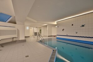 Ein Hallenbad mit gefliesten Wänden, einer Poolleiter und einer Decke mit Oberlicht.