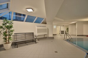 Ein moderner Poolbereich im Innenbereich mit Sitzbank, Topfpflanze und Dachfenster.